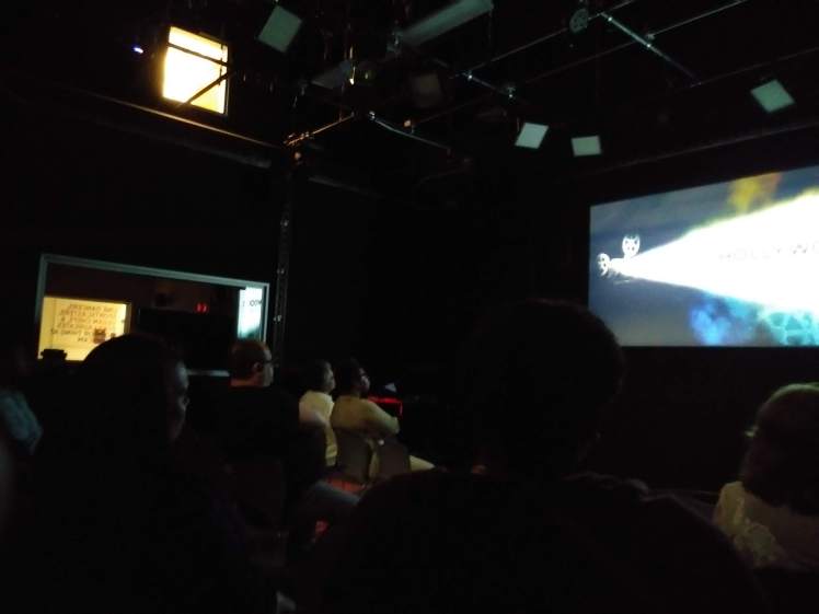 Audience viewing film on a screen in a darkened room.