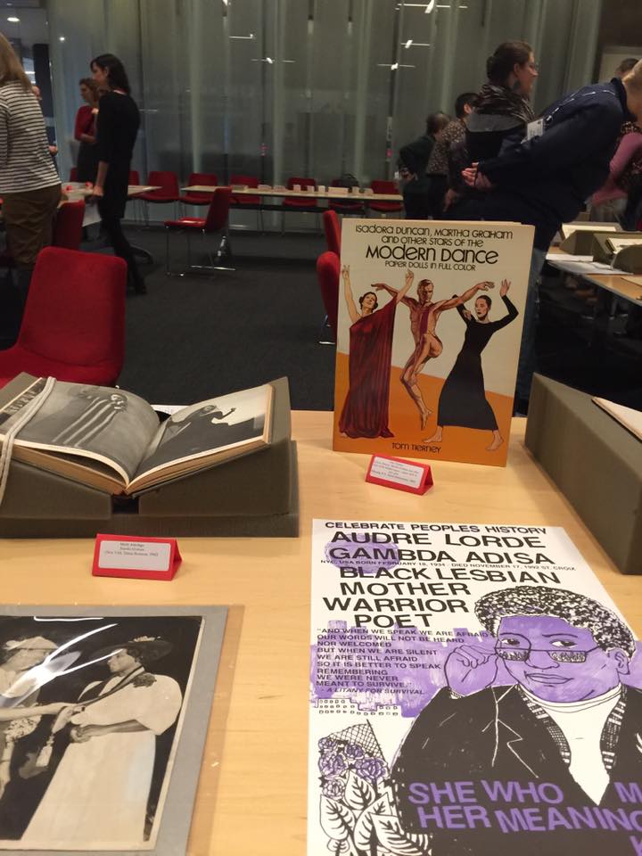 Book on modern dance, Audre Lorde poster, open book, and photo of 2 women on display on a table.